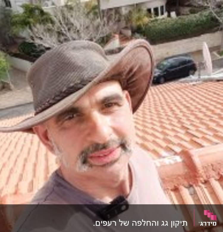 אדם עומד על גג רעפים אדום עם כובע רחב שוליים